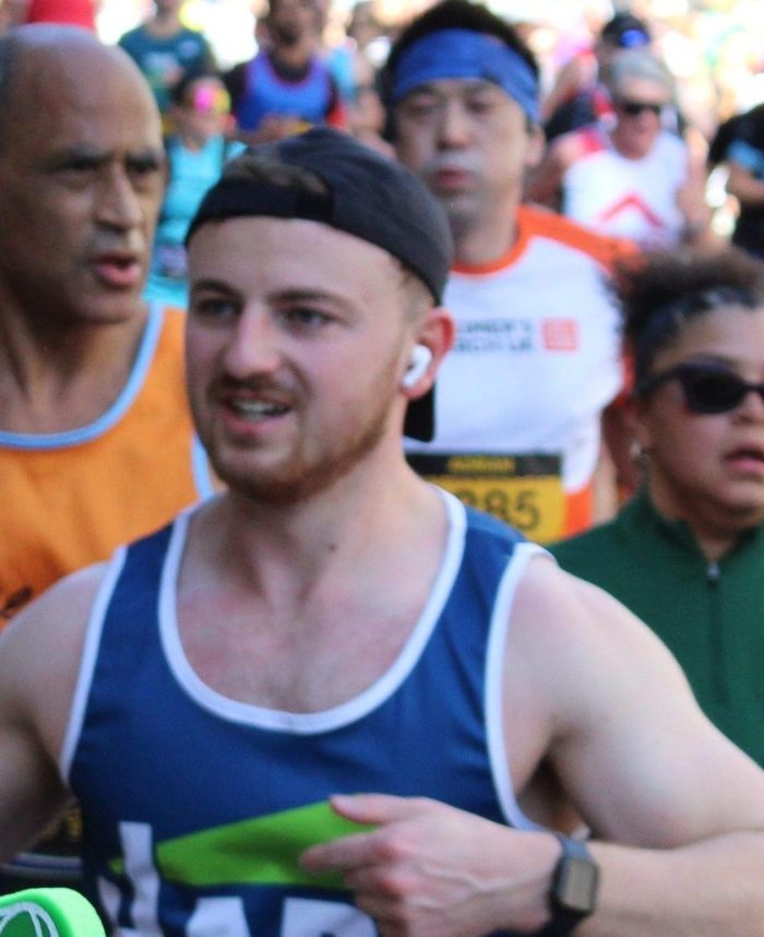 Harp Runner in a cap running and smiling alongside hundreds of people running the London Landmarks Half Marathon