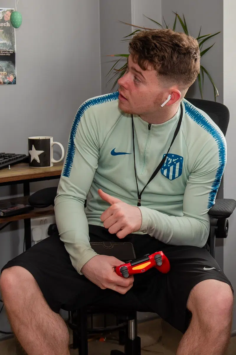 A young man sits with a games controller in his hand